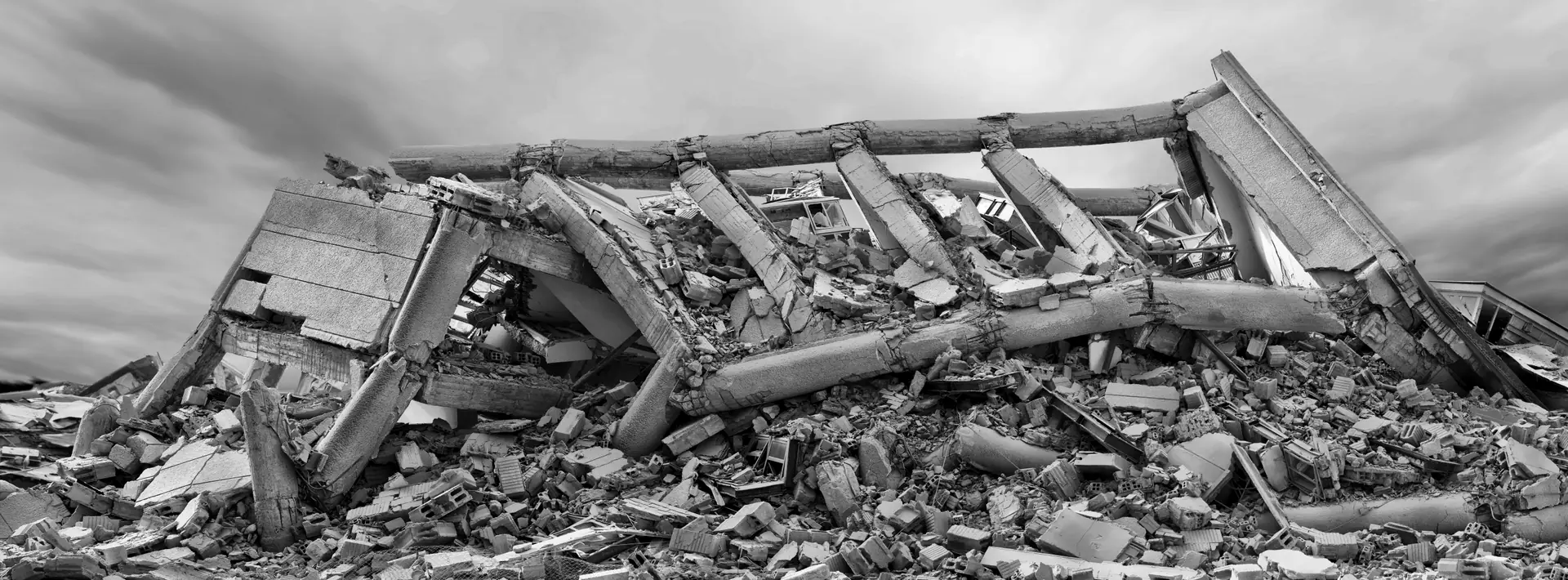 Weites Trümmerfeld eines niedergelegten Betongebäudes unter bedecktem Himmel.