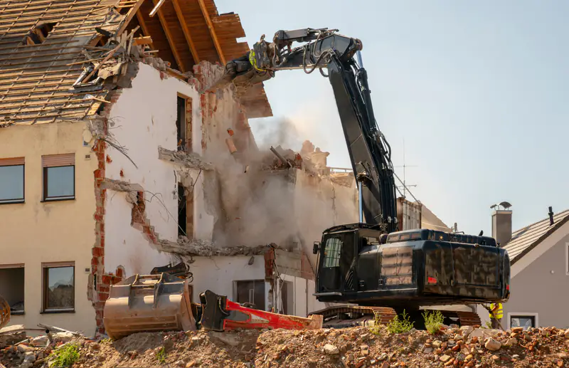 Abbruch eines Wohnhauses: Bagger mit Abbruchzange trägt die Fassade ab, Bauschutt im Vordergrund.