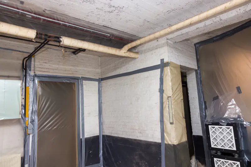 Abgeschotteter Schutzbereich einer Asbestsanierung: Wände und Türen mit Folie abgeklebt, Unterdruckgerät im Raum.